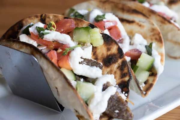 two tacos with scallions, a white sauce, and tomatoes on top