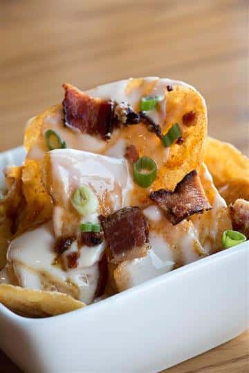 chips with a white sauce, bacon, and scallions on top