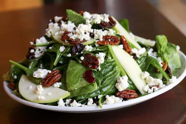 a salad with sliced apples, cheese crumbles, and nuts on top