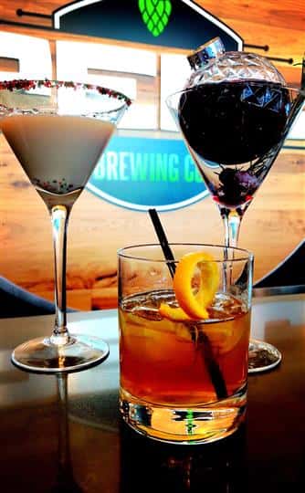 3 cocktails sitting on the bar, two in martini glasses and one in a rocks glass