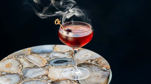 Smoked cocktail with reddish liquid and a garnish on a decorative stone table.