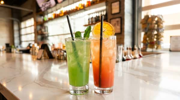 Two cocktails on a marble bar: one green with mint sprigs, the other reddish with a dried orange slice.