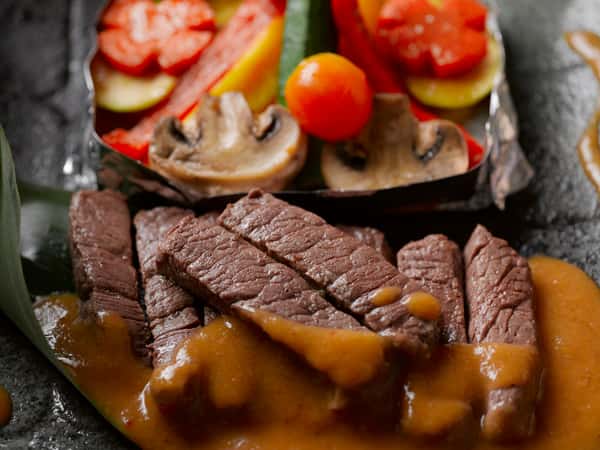Close-up of sliced steak with sauce and colorful grilled vegetables from City Limits Bar and Grill.