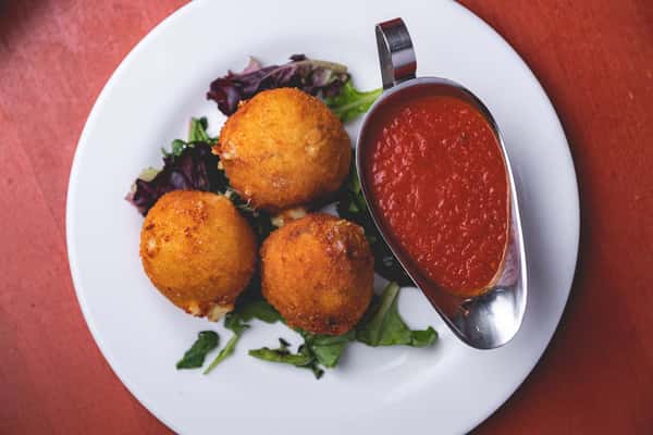 Three golden fried Italian appetizers served over greens with marinara dipping sauce at Pasta Lovers Trattoria.