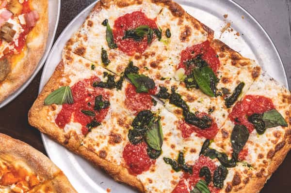 Rectangular Margherita pizza topped with fresh mozzarella, tomato sauce, basil leaves, and herbs on a golden crust at Pasta Lovers Trattoria in Midtown Manhattan.