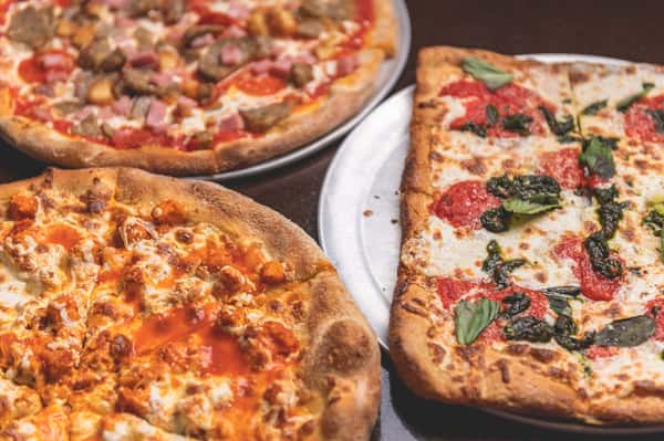 Three freshly baked Italian pizzas featuring melted mozzarella, tomato sauce, assorted toppings, and fresh basil at Pasta Lovers Trattoria in Midtown Manhattan, NYC.