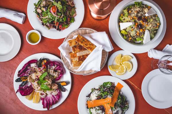 Overhead spread of colorful Italian salads, roasted vegetables, bread, and appetizers at Pasta Lovers Trattoria.
