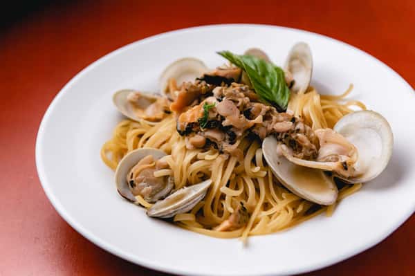 Italian linguine pasta tossed with clams, seafood, garlic, and fresh herbs, garnished with basil at Pasta Lovers Trattoria in Times Square, NYC.