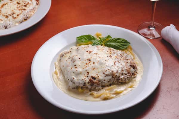 Italian entrée topped with melted cheese and herbs, served in a creamy sauce with fresh basil garnish at Pasta Lovers Trattoria in Midtown Manhattan, NYC.