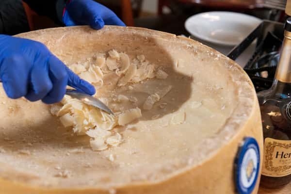 Freshly cooked pasta being tossed inside a large Parmesan cheese wheel by a chef wearing blue gloves at Pasta Lovers Trattoria in Midtown Manhattan, NYC.