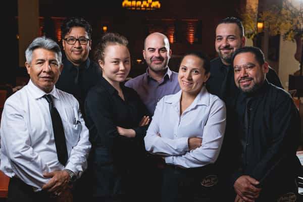 Five smiling Pasta Lovers Trattoria team members standing together inside the restaurant, dressed in professional attire, showcasing the welcoming hospitality of the family-owned Italian restaurant in Midtown Manhattan, NYC.