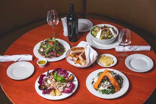 Assortment of Italian salads, appetizers, and bread served on a dining table with wine glasses at Pasta Lovers Trattoria.