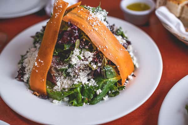 Fresh mixed greens topped with roasted carrots, crumbled cheese, and herbs, served on a white plate at Pasta Lovers Trattoria in Times Square, NYC.