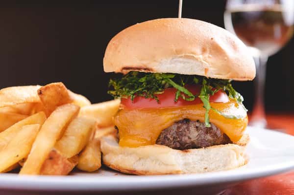 Juicy cheeseburger topped with fresh lettuce, tomato, and melted cheese on a toasted bun, served with golden French fries at Pasta Lovers Trattoria in Midtown Manhattan.
