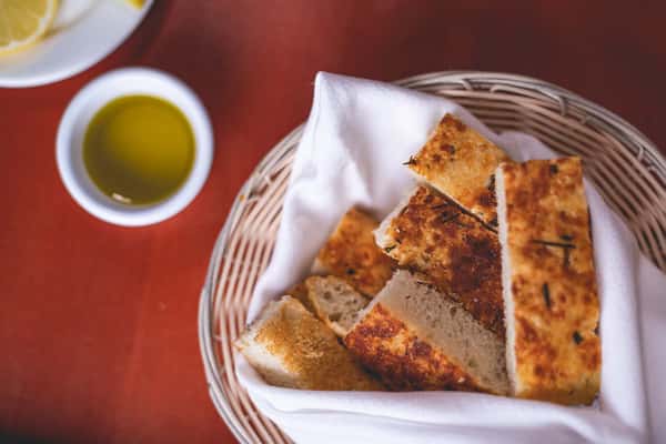 Toasted Italian flatbread cut into triangles and served in a bread basket with olive oil at Pasta Lovers Trattoria in Midtown NYC.
