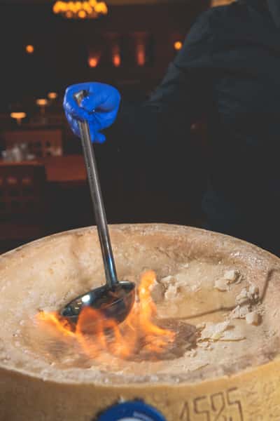 Dramatic tableside pasta preparation featuring flames rising from a Parmesan cheese wheel as a chef holds a long metal utensil at Pasta Lovers Trattoria in Midtown Manhattan.