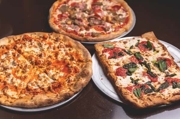 Three freshly baked Italian pizzas featuring assorted meat toppings, melted cheese, tomato sauce, and fresh basil, served at Pasta Lovers Trattoria in Times Square, NYC.