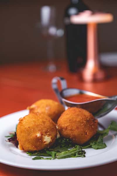 Close-up of golden-brown fried Italian appetizers served with a side of marinara dipping sauce.