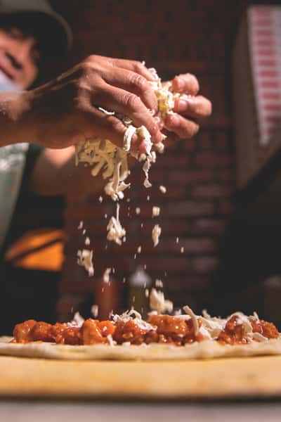 Freshly grated Parmesan cheese falling over a plate of pasta with tomato sauce, highlighting the preparation of Italian cuisine at Pasta Lovers Trattoria in Midtown Manhattan, NYC.