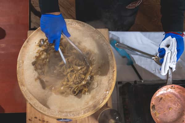 Chef preparing fresh Italian pasta inside a hollowed-out Parmesan cheese wheel, using metal utensils to mix the pasta with melted cheese at Pasta Lovers Trattoria in Times Square, NYC.