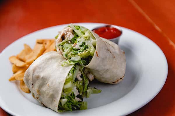 Freshly prepared chicken wrap filled with crisp lettuce and vegetables, served on a white plate with a side of tomato sauce at Pasta Lovers Trattoria in Midtown Manhattan, NYC.