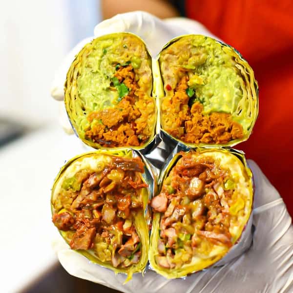 Four burrito halves held in gloved hands, filled with guacamole, rice, and either seasoned ground meat or chopped grilled pork.