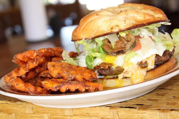burger on a bun topped with mushrooms, lettuce and cheese served with home fries
