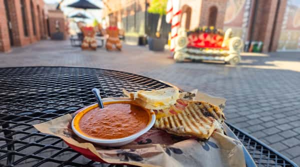 Grilled panini sandwich served with a creamy bowl of tomato soup on an outdoor café patio, creating a cozy lunch experience in a charming downtown setting.
