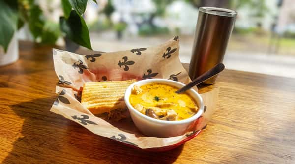 Grilled panini served with a creamy bowl of soup and a stainless steel tumbler on a sunlit café table, perfect for a fresh and comforting lunch.