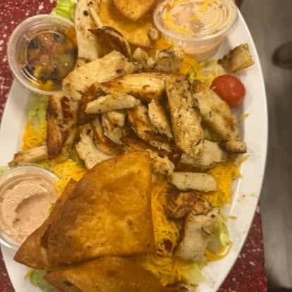 A plate with grilled chicken strips, tortilla chips, shredded cheese, and two dipping sauces.