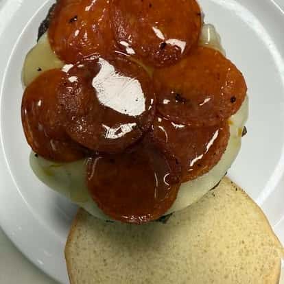 A burger with melted mozzarella cheese topped with slices of pepperoni, placed on a plain sandwich bun.