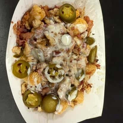 A plate of cheesy tater tots topped with crispy bacon and jalapeño slices.