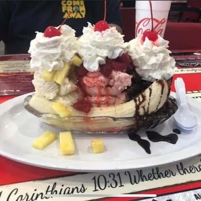 Banana split topped with whipped cream, cherries, chocolate syrup, and chunks of pineapple served in a glass dish.