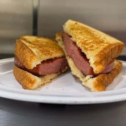 A grilled sandwich cut in half, featuring slices of ham between two pieces of golden toasted bread.