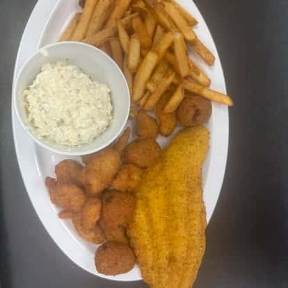 A plate of golden fried fish fillets, hush puppies, crispy fries, and a side of creamy coleslaw.