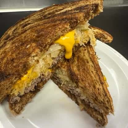 Grilled sandwich with melted cheddar cheese, sauerkraut, and ground beef on toasted rye bread, cut in halves on a white plate.