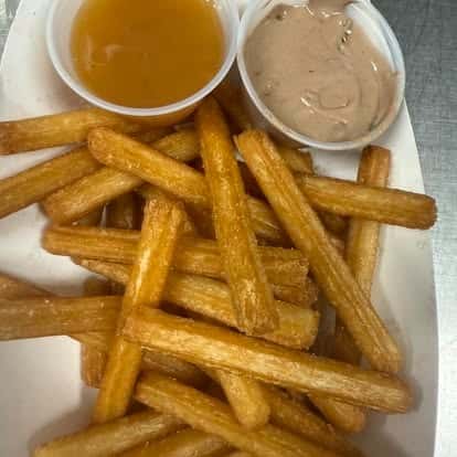 A serving of crispy fries accompanied by two dipping sauces, one brown and one light-colored.