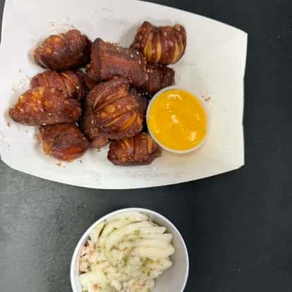 A plate of crispy, seasoned pretzel bites served with a side of mustard and a small bowl of creamy coleslaw.