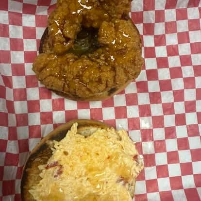 A close-up of a sandwich featuring a crispy fried chicken patty with honey drizzled on top, and a layer of melted cheese on the bottom bun.