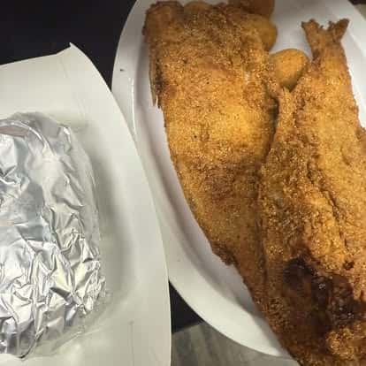 A plate with two crispy fried fish fillets and a foil-wrapped baked potato on the side.