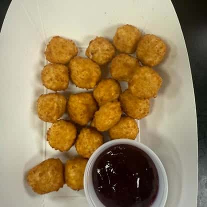 A portion of golden, breaded chicken nuggets served with a side of dipping sauce in a small container.