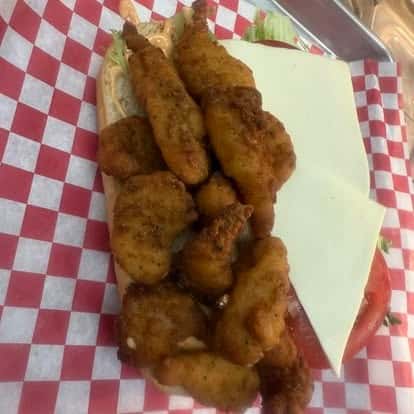 A sandwich with fried chicken tenders, slices of cheese, and fresh tomatoes, served in a red checkered basket.
