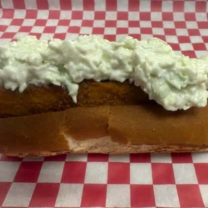 A sandwich with a fried item inside, topped with a generous amount of creamy coleslaw, all served on a soft bun.