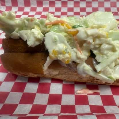 A sandwich filled with cole slaw and served in a soft bun with a red and white checkered paper lining.