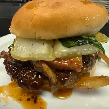 A close-up of a burger with a juicy beef patty, grilled onions, melted cheese, and a sweet sauce, all served in a soft bun.