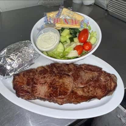 A plate of grilled steak slices served with a side of fresh salad, crackers, and a foil-wrapped baked potato.