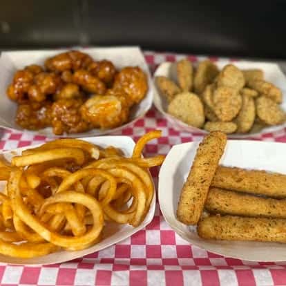 Assorted appetizers including buffalo wings, fried pickles, curly fries, and mozzarella sticks on a red and white checkered tray.