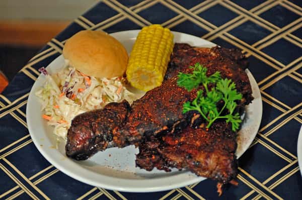 two racks of ribs with a side of corn, coleslaw, and biscuit