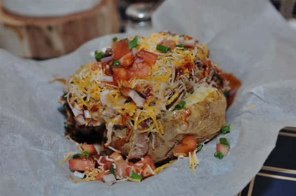 baked potato topped with pulled pork, tomatoes, shredded cheese, onions, and chives