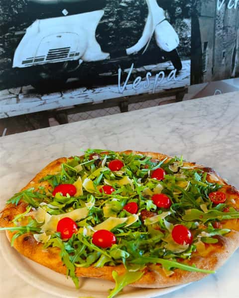 pizza with arugula, shaved cheese, and tomatoes